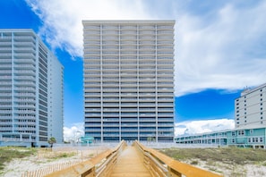 A modern hotel with a central atrium, multiple floors, and a wooden walkway leading to the entrance. - Phoenix Gulf Shores Ii 1403 3 Bedroom Condo (Gulf Shores)