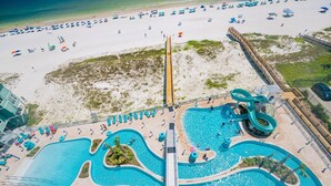 An aerial view of a beach resort with multiple swimming pools, a water slide, and beach umbrellas. - Phoenix Gulf Shores Ii 803 3 Bedroom Condo (Gulf Shores)