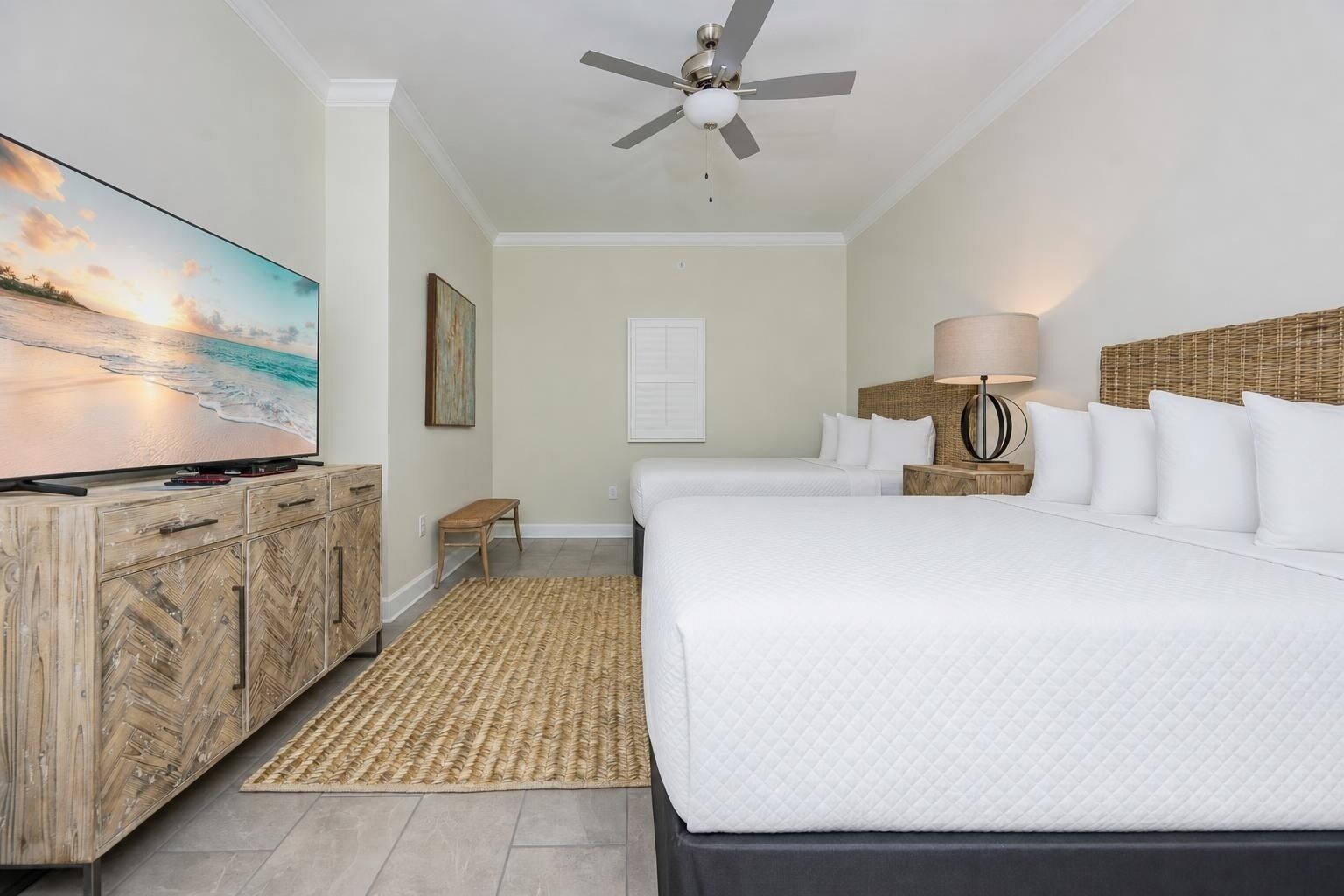 A hotel room with a large bed, a television, a ceiling fan, a bedside lamp, and a view of the beach.