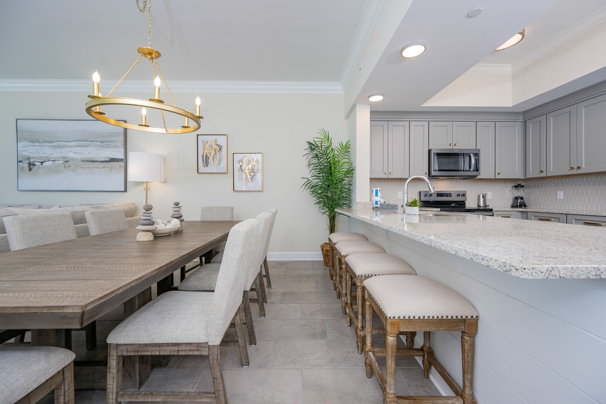 A modern kitchen with a large island, grey cabinets, and a chandelier.