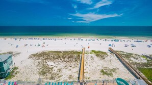 A beach with a wooden boardwalk, beach umbrellas, and a lifeguard tower. - Phoenix Gulf Shores Ii 803 3 Bedroom Condo (Gulf Shores)