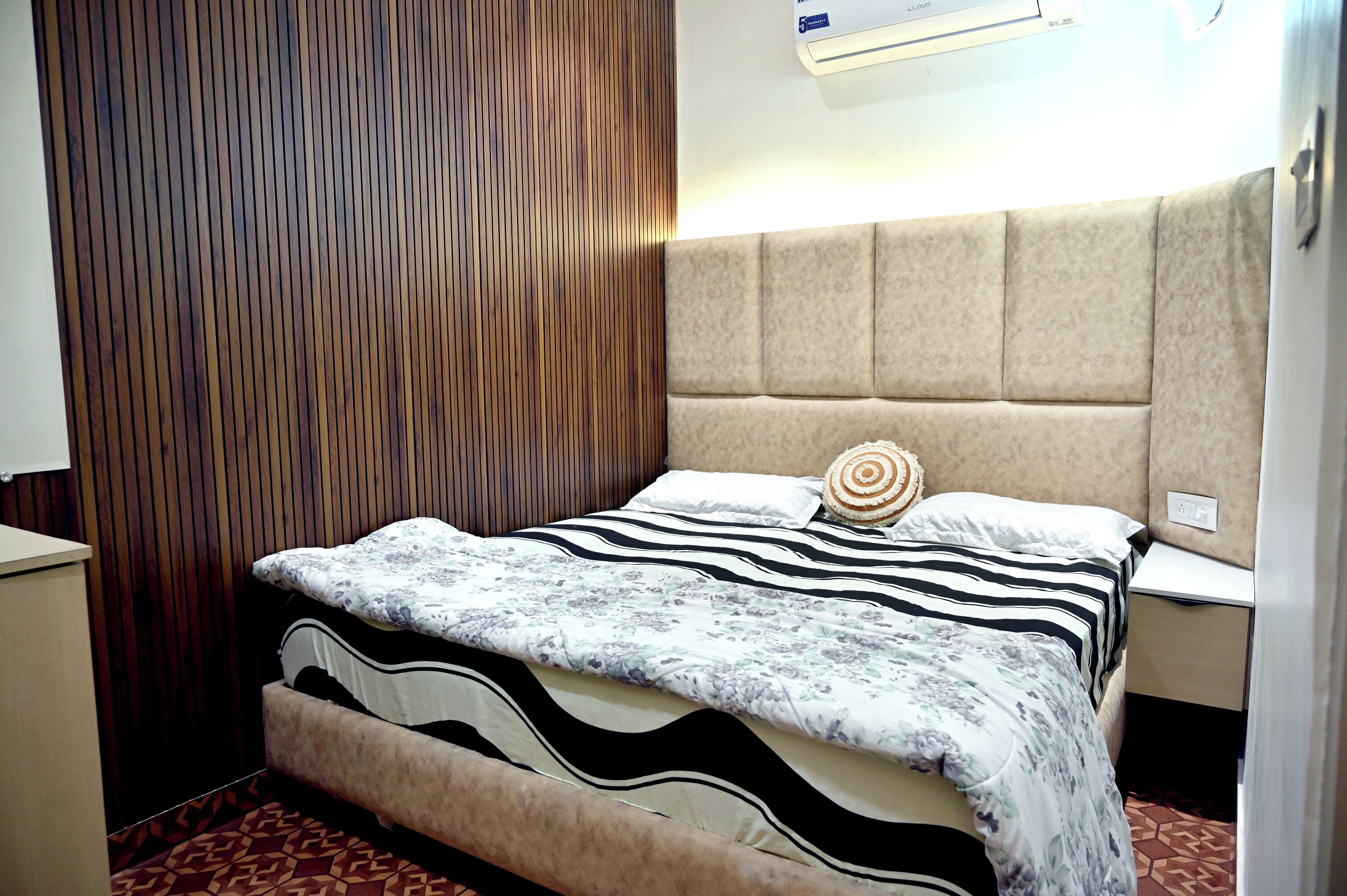 A bedroom with a bed, a headboard, a bedside table, and a wall-mounted air conditioner.