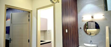 Une salle de bain moderne avec un grand miroir, une horloge murale ronde et un lavabo avec un meuble-vasque en bois.