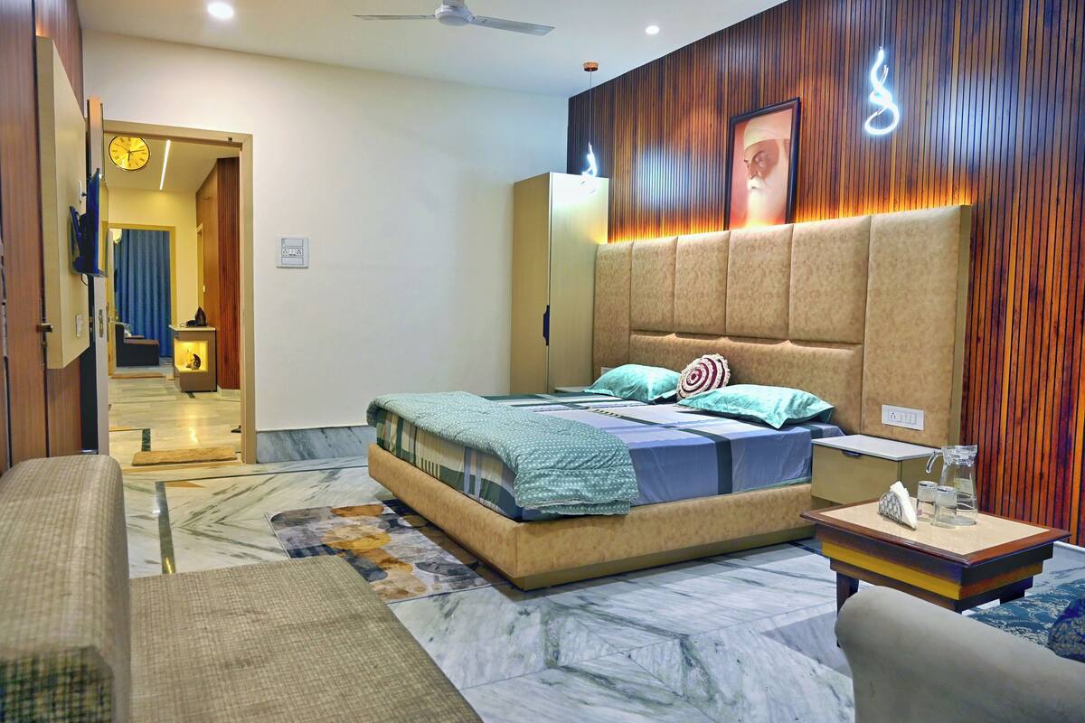 A modern bedroom with a large bed, a bedside table, a nightstand, a ceiling fan, and a wall-mounted light fixture.