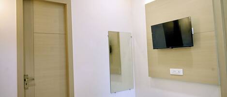 A bedroom with a wooden wardrobe, a bed with patterned bedding, a wall-mounted TV, and a mirror.