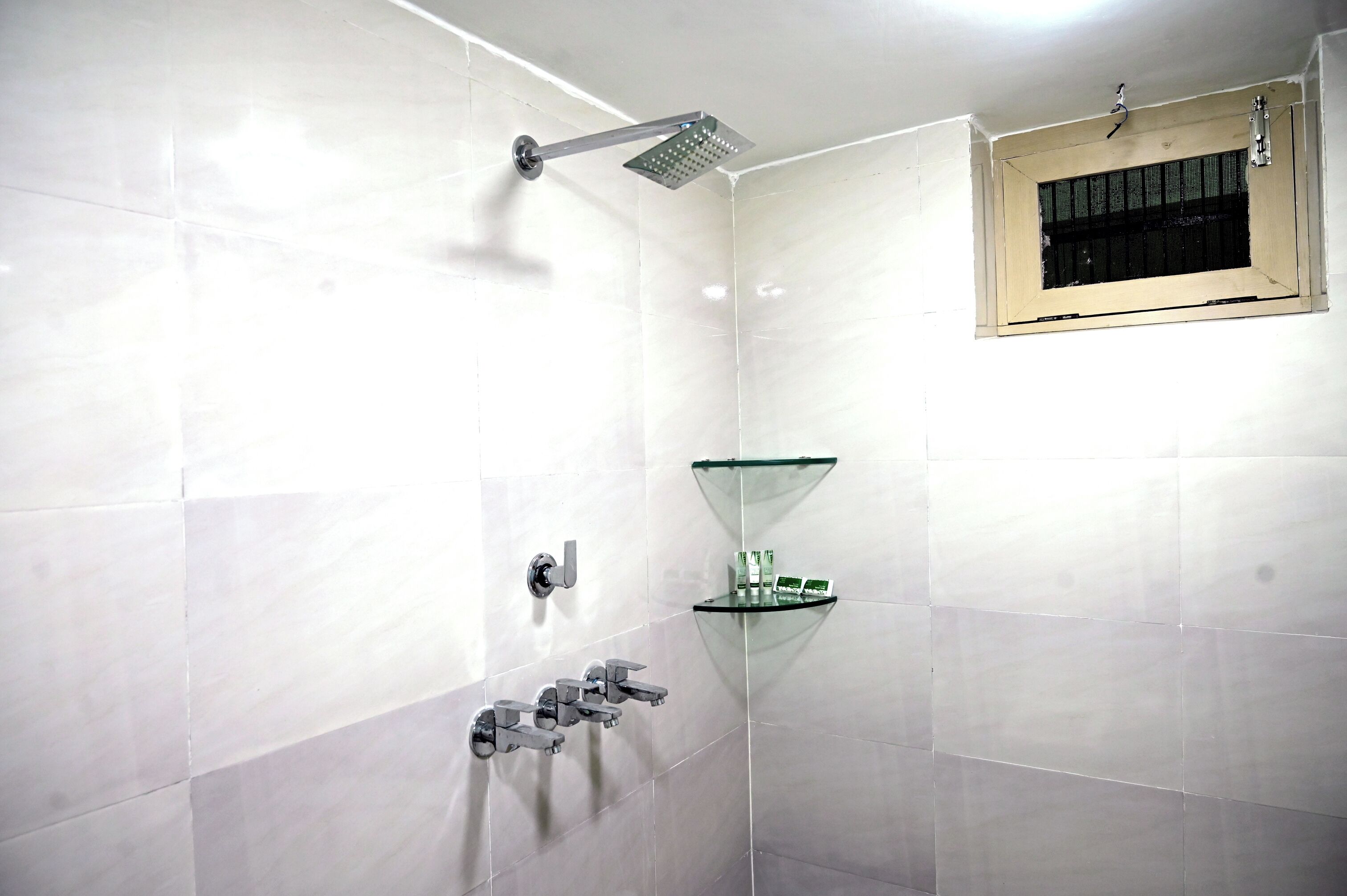 Une salle de bain moderne avec des carreaux blancs, une douche en verre et une petite étagère contenant des articles de toilette.