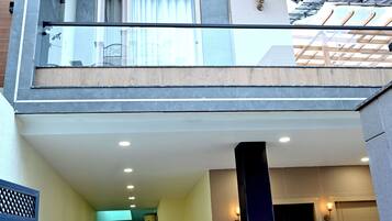 Un edificio de dos pisos con un balcón, una entrada cubierta y un pasillo que lleva a una puerta.