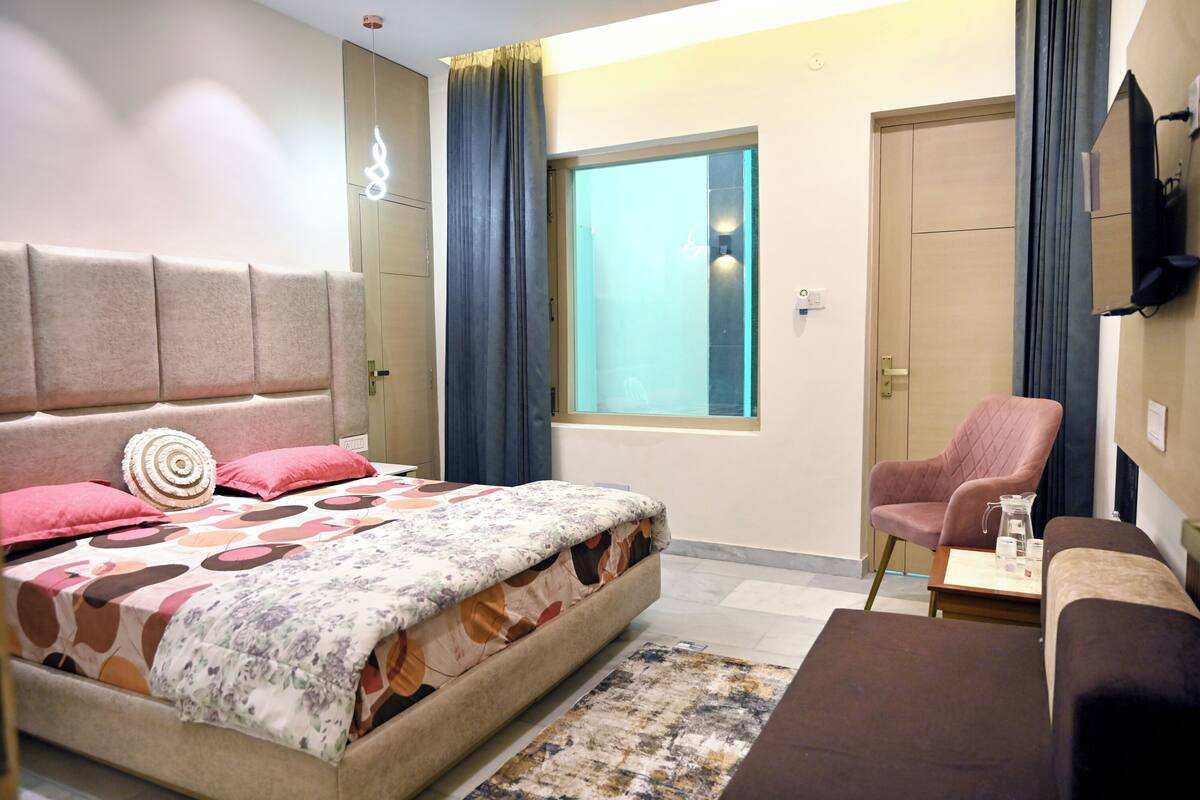 A bedroom with a bed, a chair, a small table, a window, and a TV.