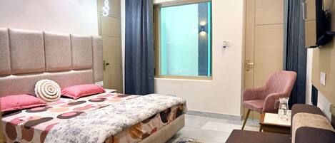 Un dormitorio con cama, una silla, una mesita, una ventana y un televisor.