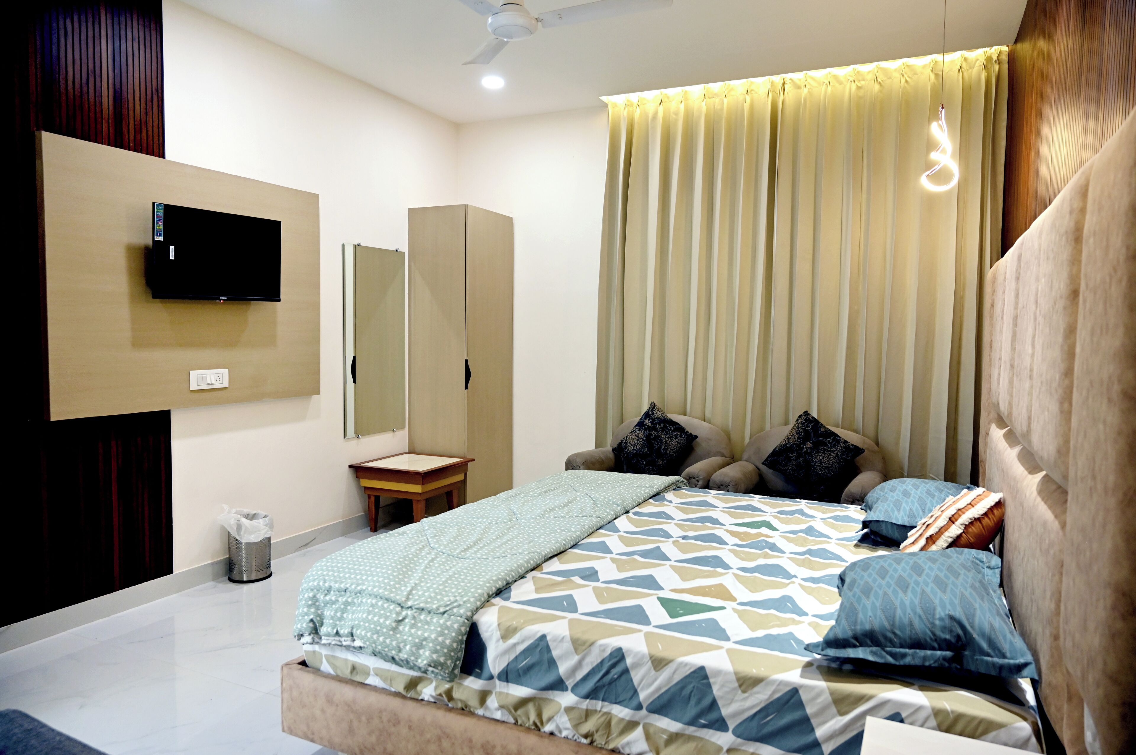 A bedroom with a bed, a TV mounted on the wall, a bedside table, and a mirror.