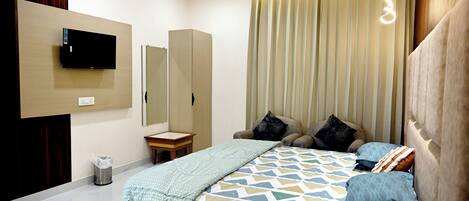 A bedroom with a bed, a TV mounted on the wall, a bedside table, and a mirror.