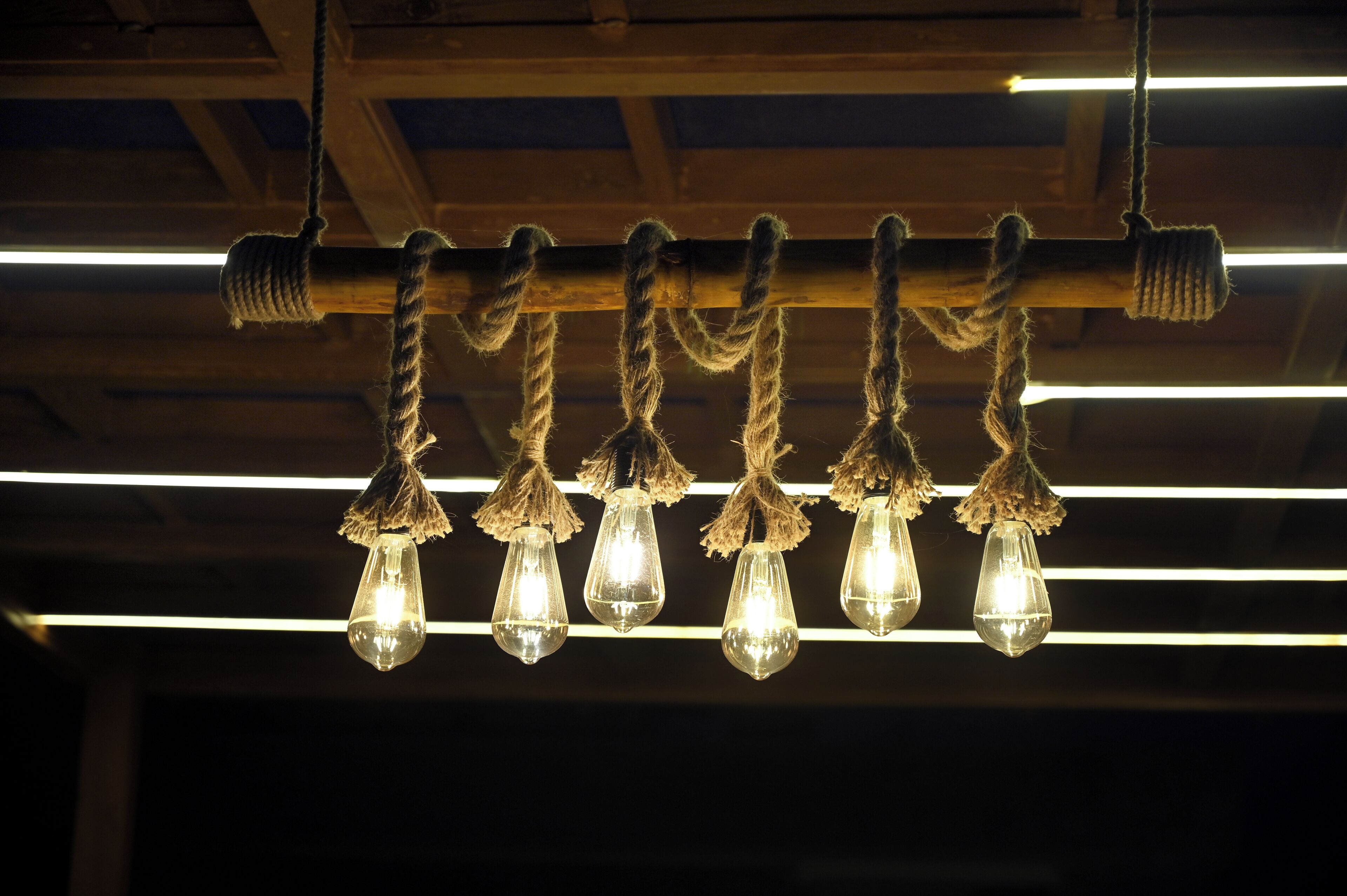 A ceiling with exposed wooden beams and hanging light fixtures with tassels.
