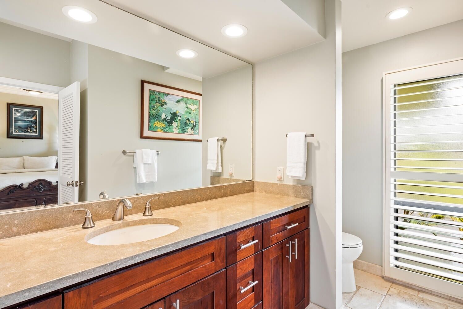 A bathroom with a large mirror, two sinks, a wooden vanity, and a toilet.