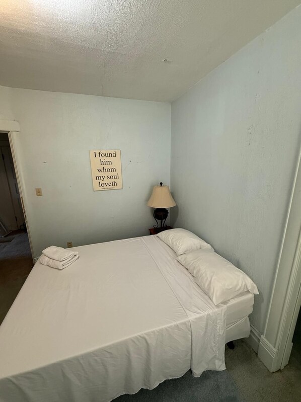 Ein Einzelbett in einem Zimmer mit einem an der Wand befestigten Schild, einer Lampe und einer Tür.