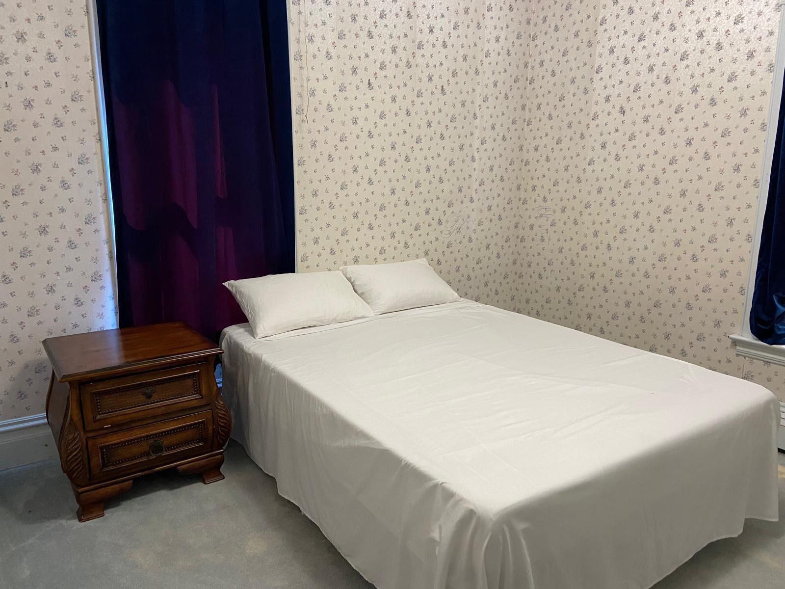 Un dormitorio con una cama individual, una mesita de noche de madera y papel tapiz con motivos florales.