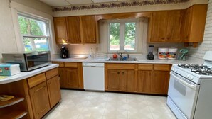 Una cocina con armarios de madera, microondas, lavavajillas, estufa y ventana con vista a árboles.