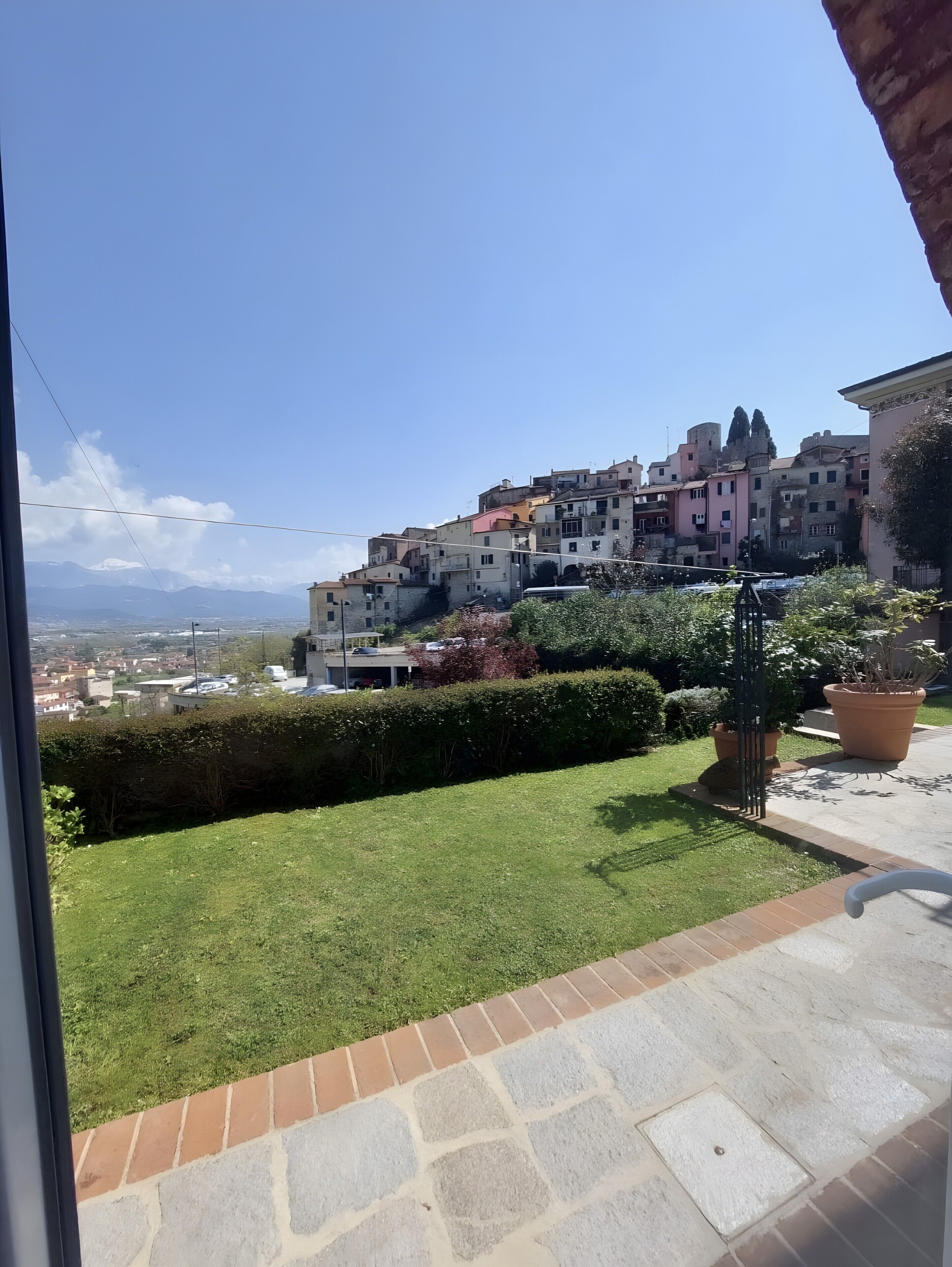 A balcony with a view of a hillside town, a grassy area, and potted plants.