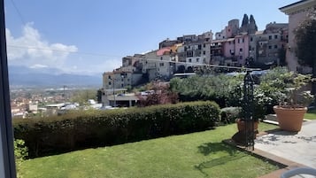 A balcony with a view of a hillside town, a grassy area, and potted plants.