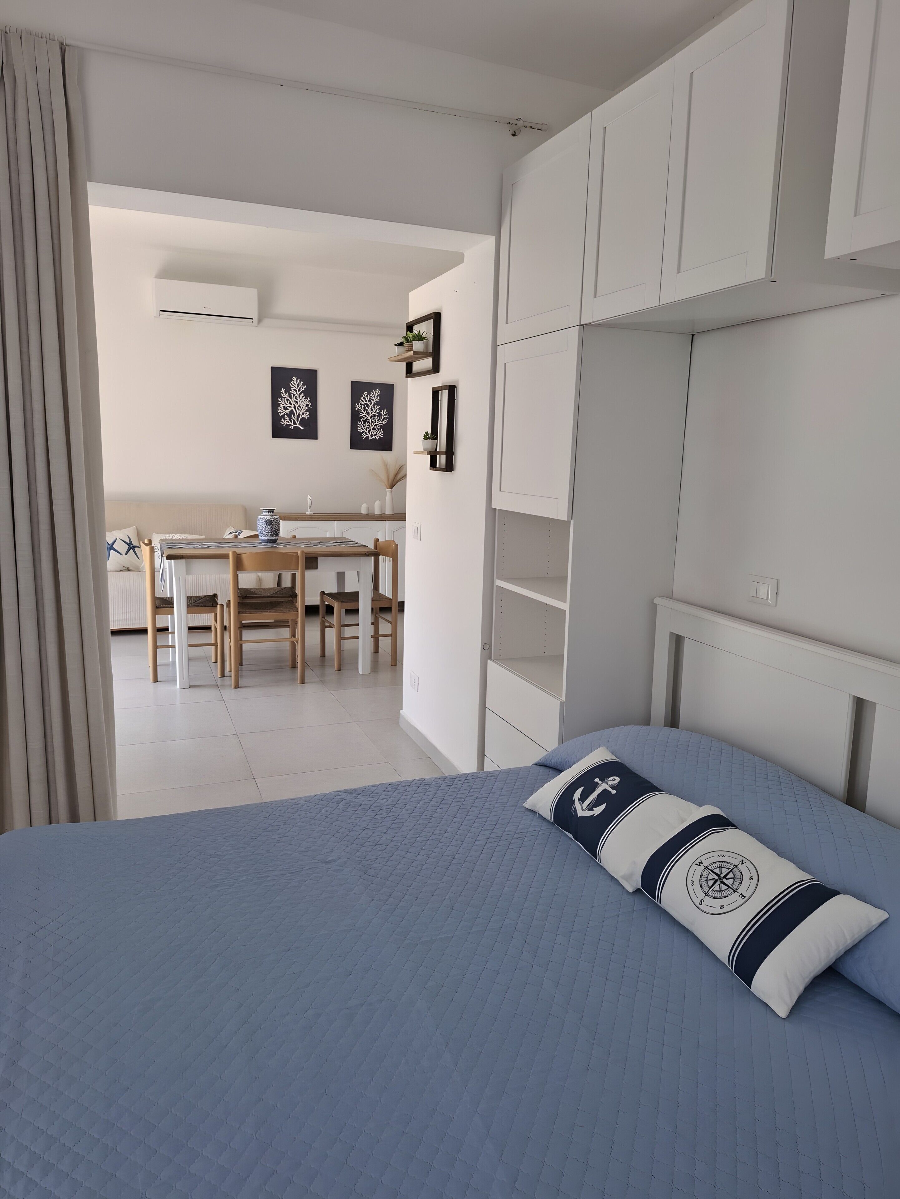A bedroom with a bed, a desk, and chairs in the background.