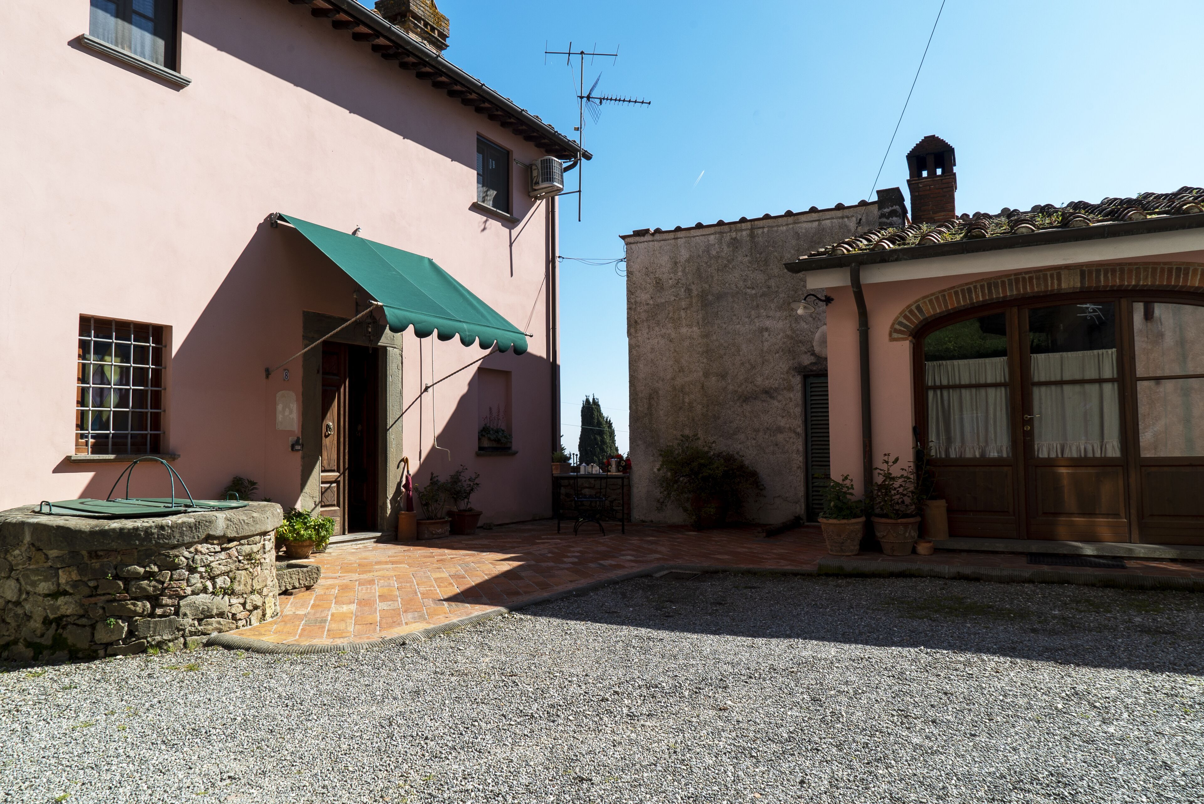 Un patio con un pozo de piedra, un toldo verde y un edificio rústico con techo de tejas.