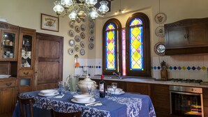 A dining area with a table set for four, a chandelier, stained glass windows, and a kitchen with a stove and oven.