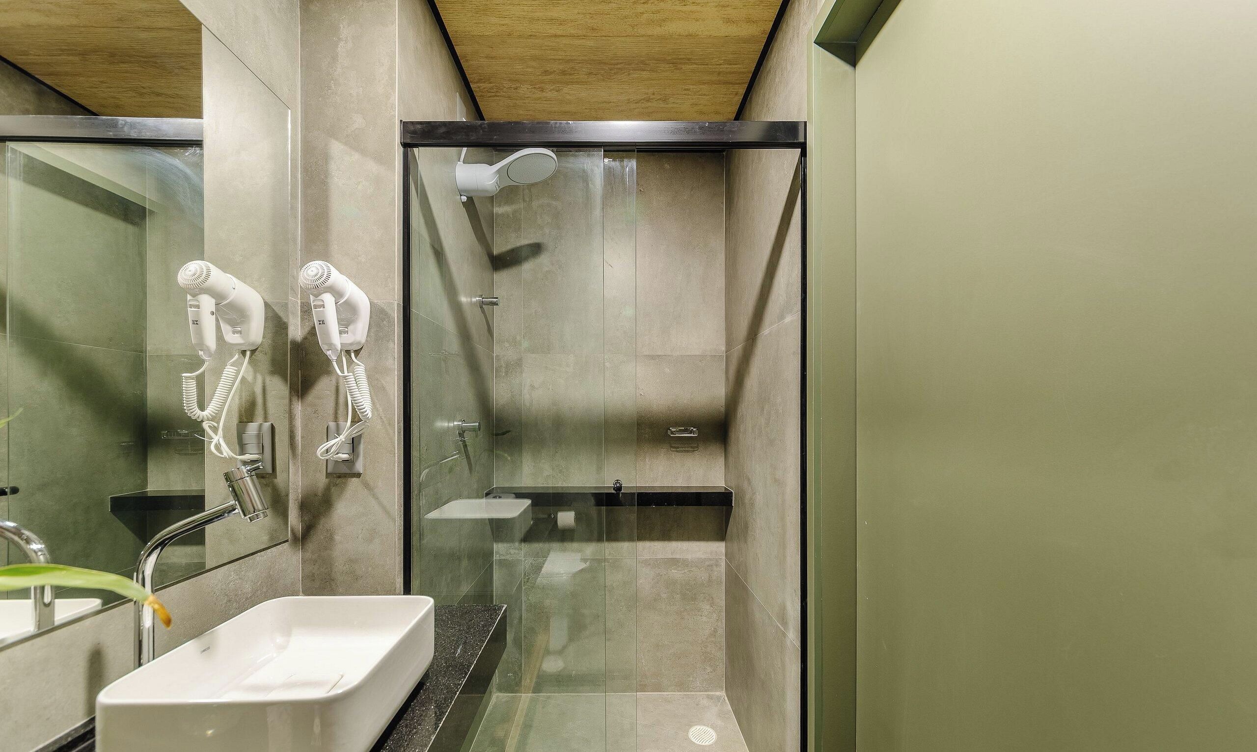A modern bathroom with a glass-enclosed shower, a white sink, and two hair dryers mounted on the wall.