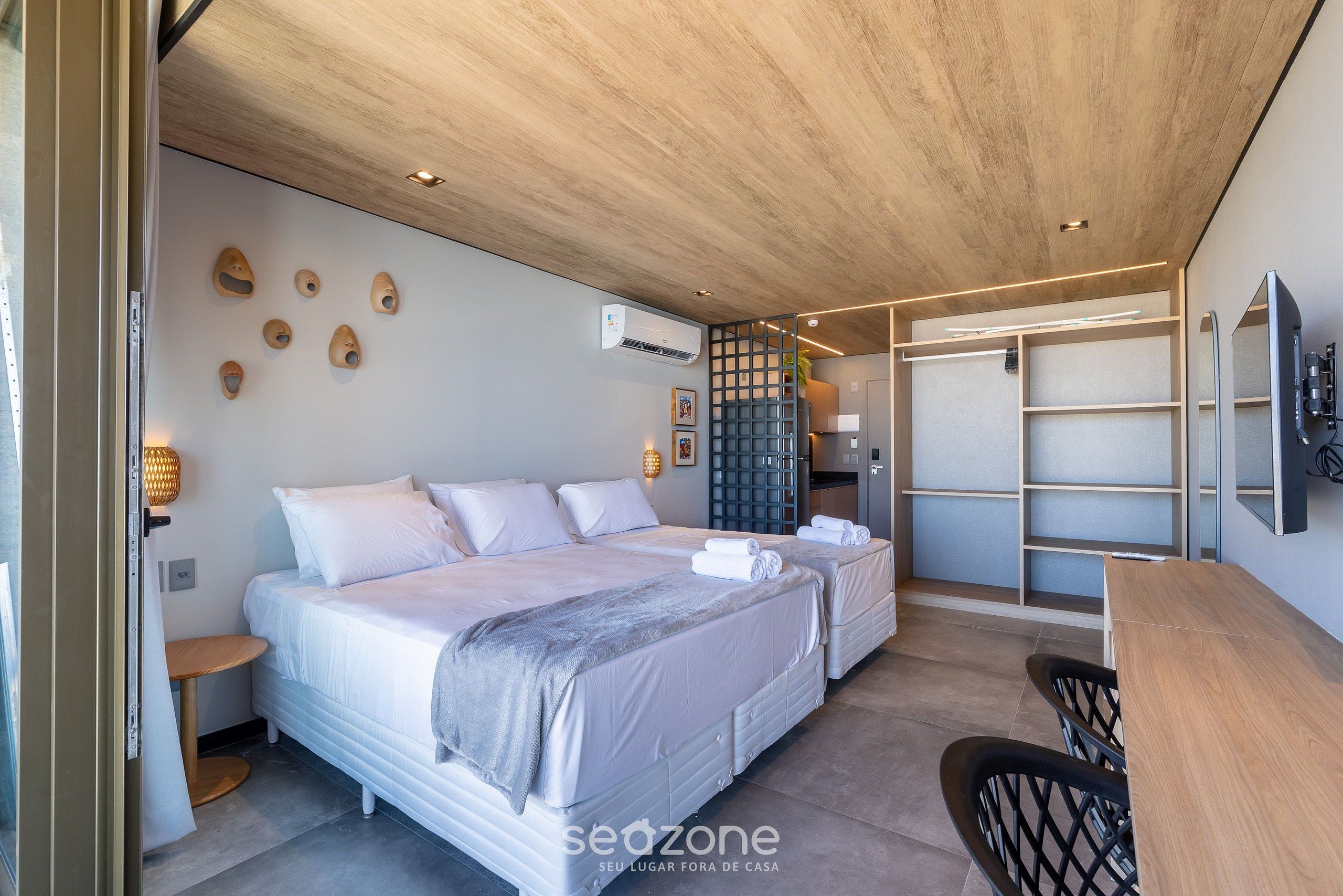 A modern hotel room with two beds, a desk, and a wardrobe.