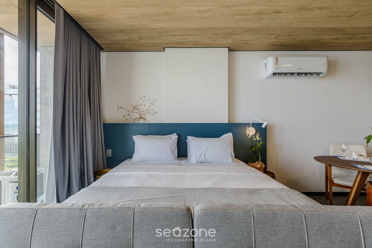 Una habitación de hotel moderna con una cama grande, una mesita pequeña y un ventanal con cortinas.