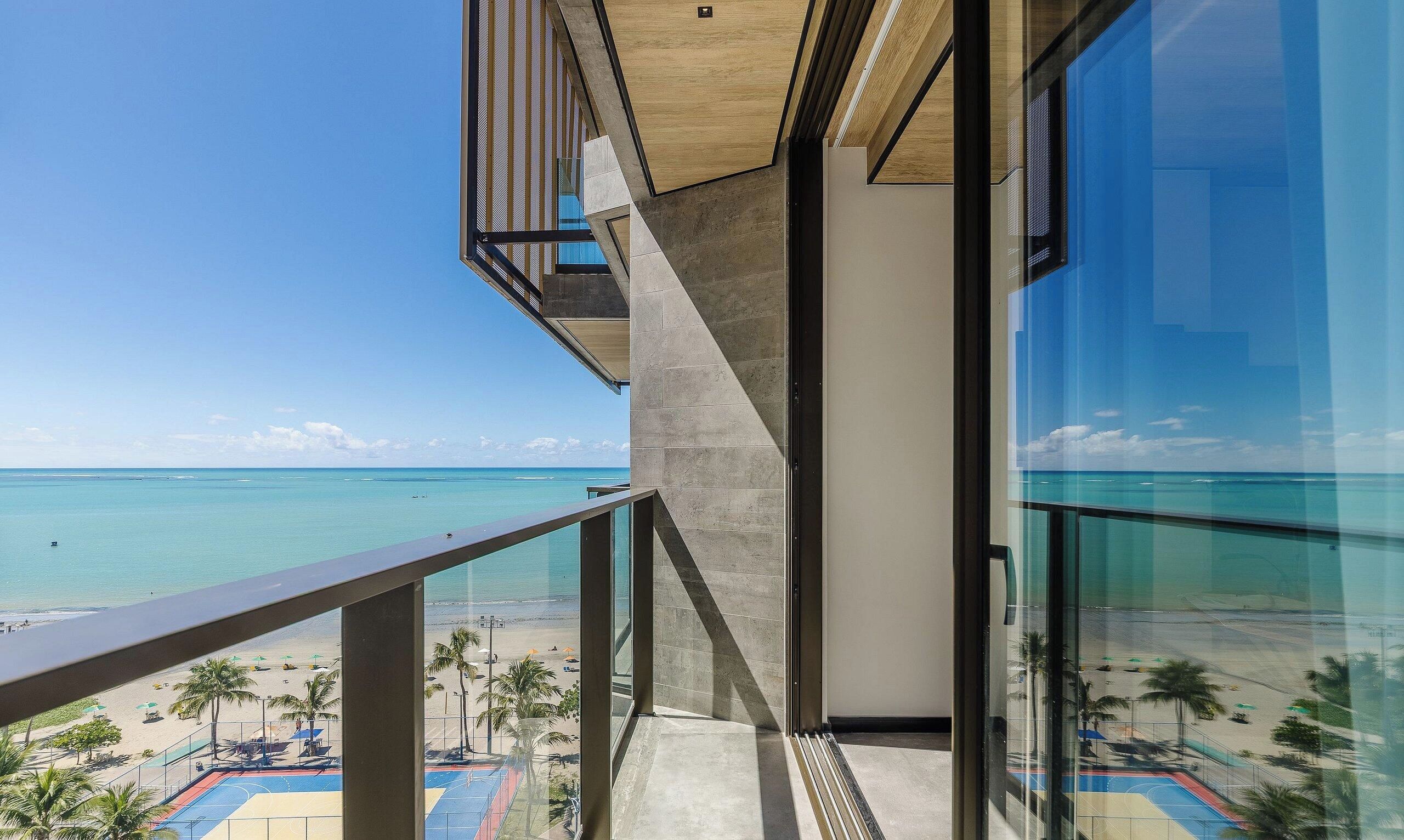 A modern building with a balcony overlooking a beach and ocean.