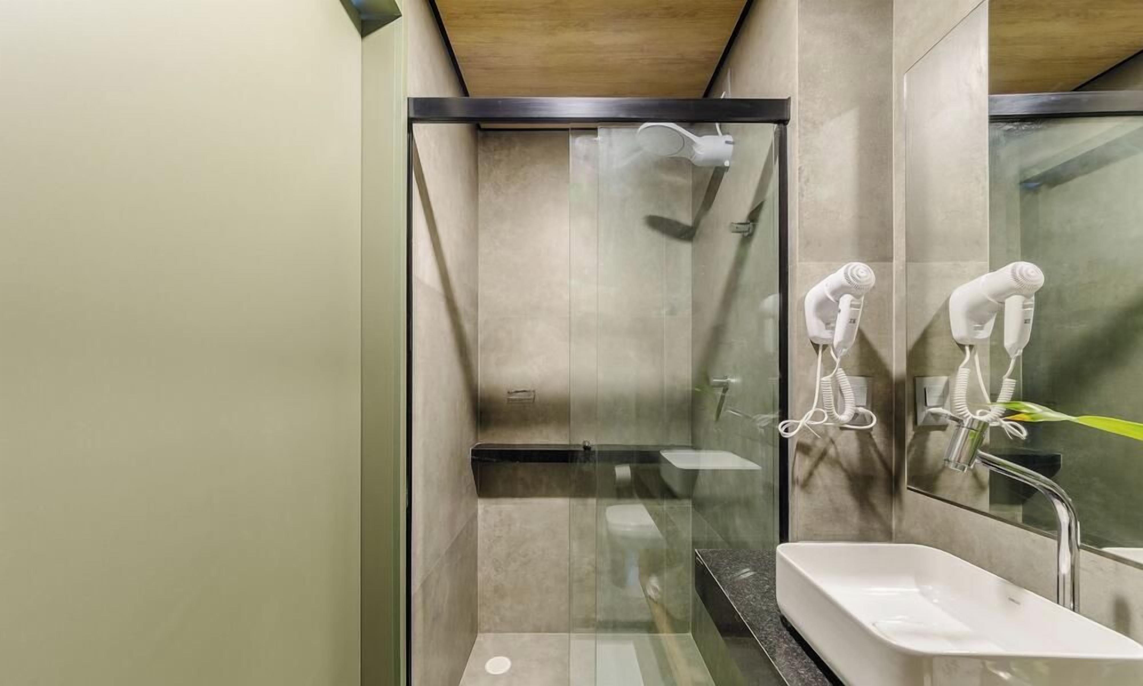 A modern bathroom with a glass-enclosed shower, a sink, and two hair dryers mounted on the wall.