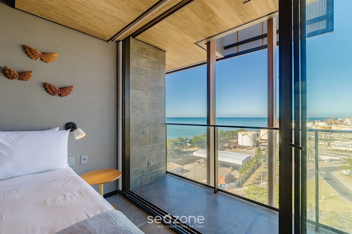 Une chambre moderne dotée d’une grande fenêtre donnant sur un paysage urbain et la mer.