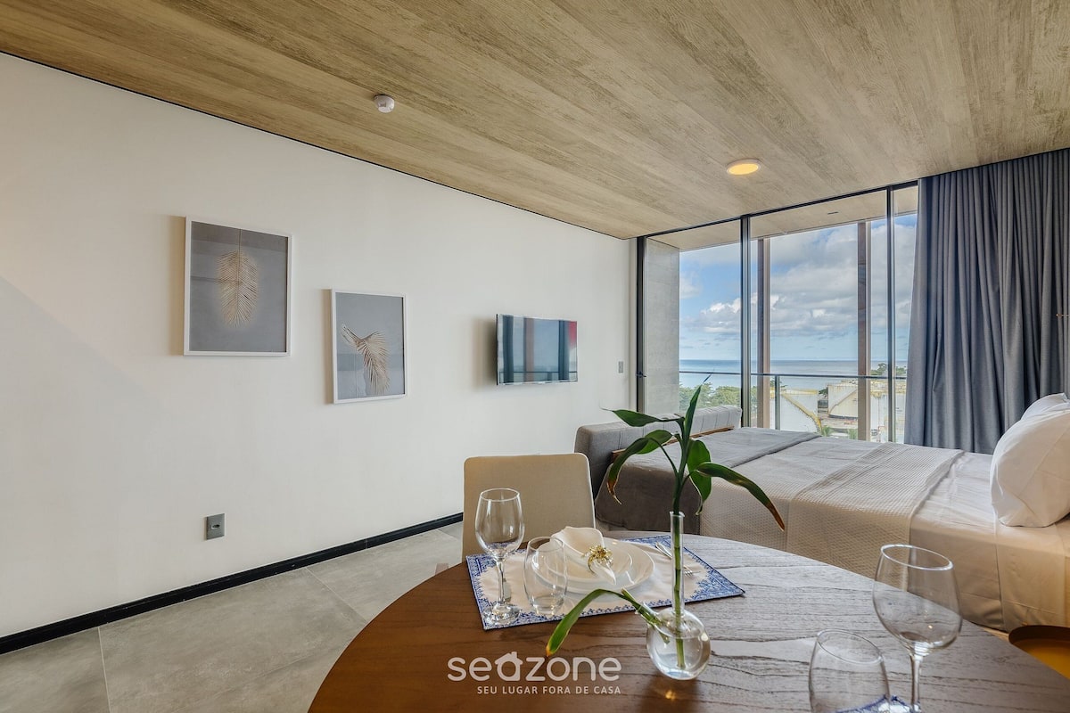 Una habitación de hotel moderna con una mesa de comedor preparada para dos personas, un ventanal con vistas y obras de arte en las paredes.