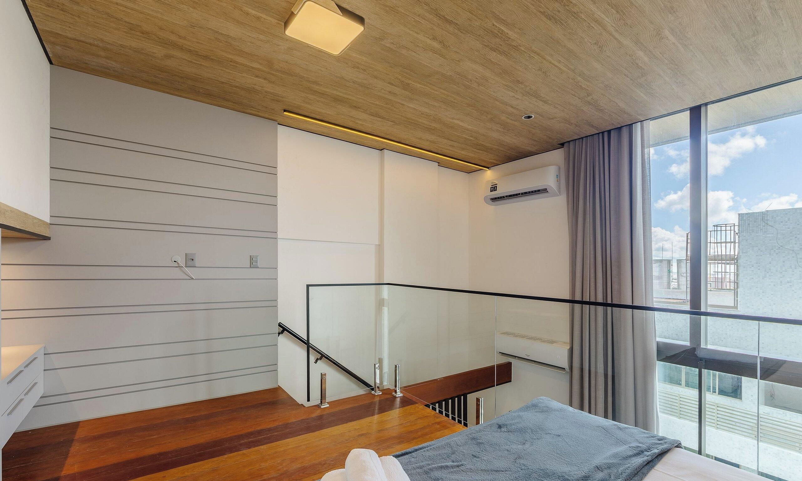 Ein modernes Interieur mit einer Holztreppe, einem Glasgeländer und Blick auf die Stadt durch große Fenster.