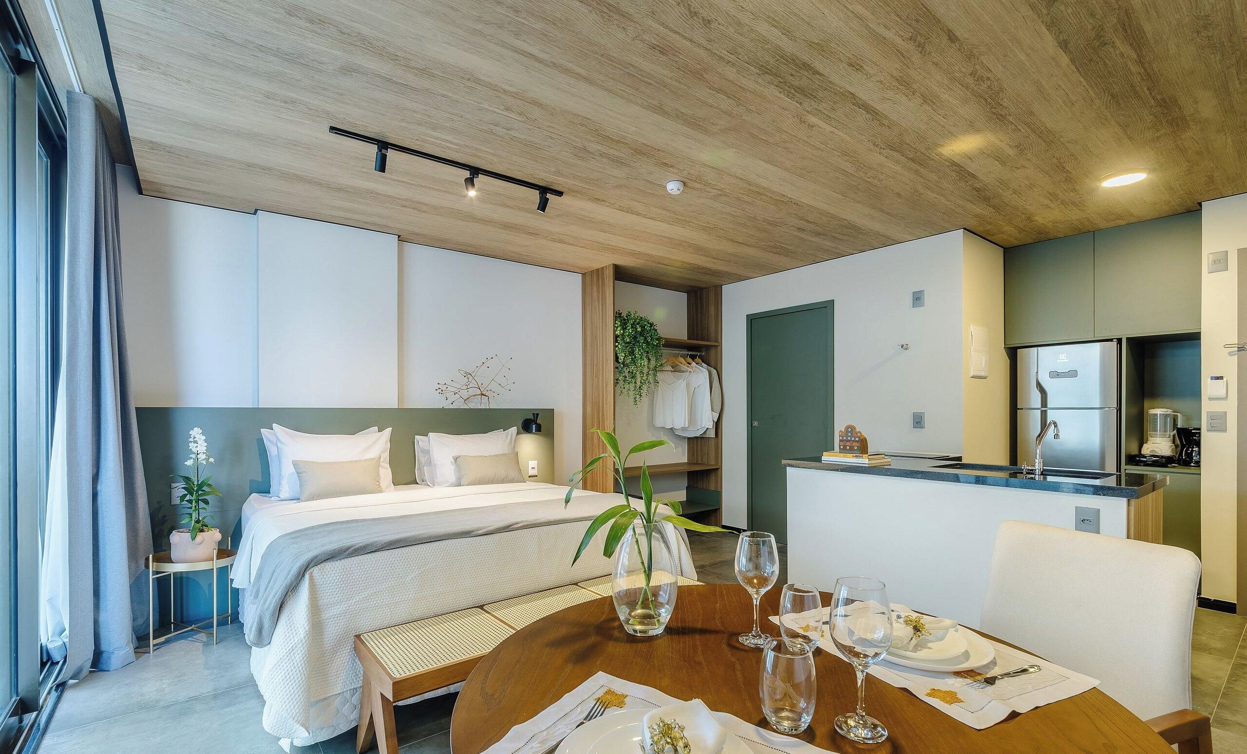 Habitación de hotel con cama, una mesa de comedor dispuesta con platos, vasos y un jarrón de flores.