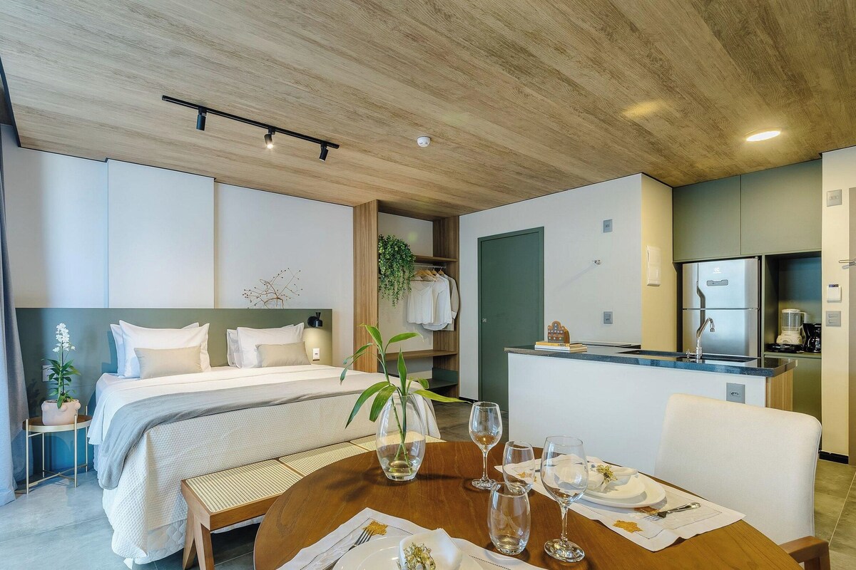 A hotel room with a bed, bedside table, a dining table set for two, a kitchen area, and a bathroom.