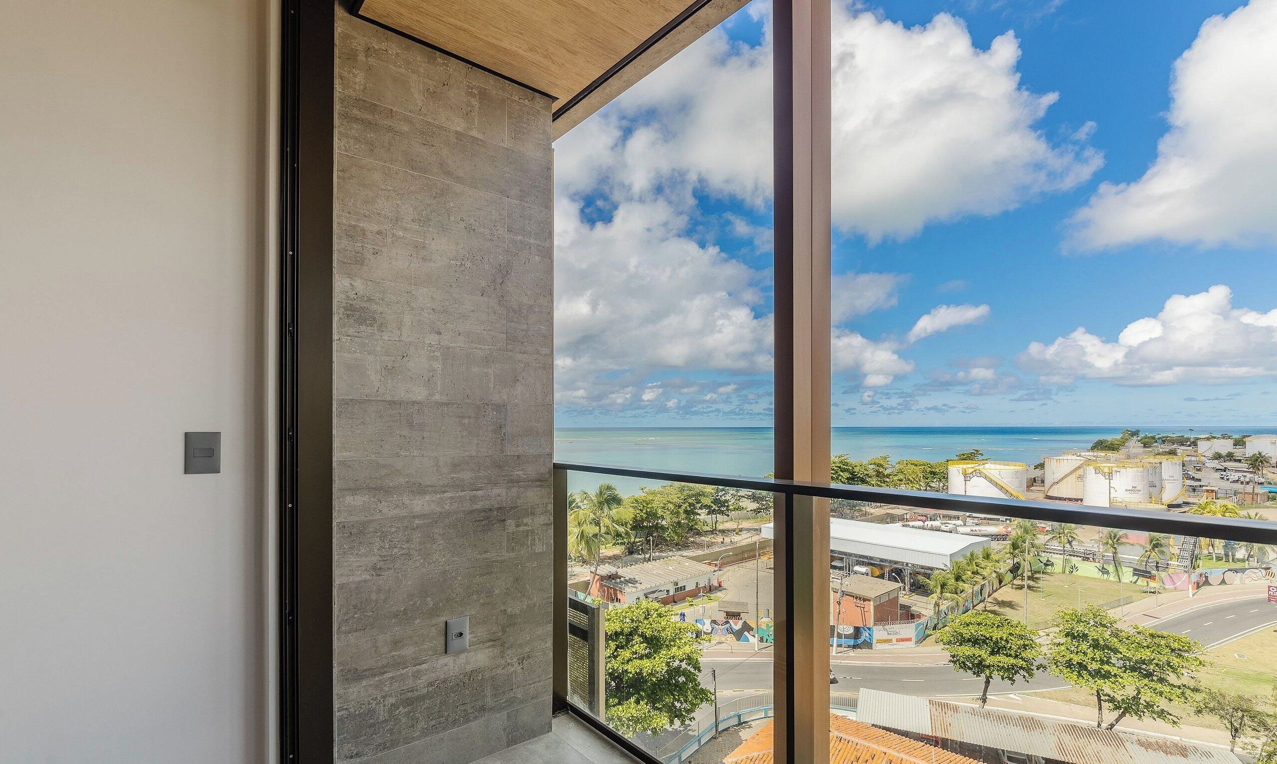 A room with a large window overlooking a coastal view, including a beach and industrial buildings.