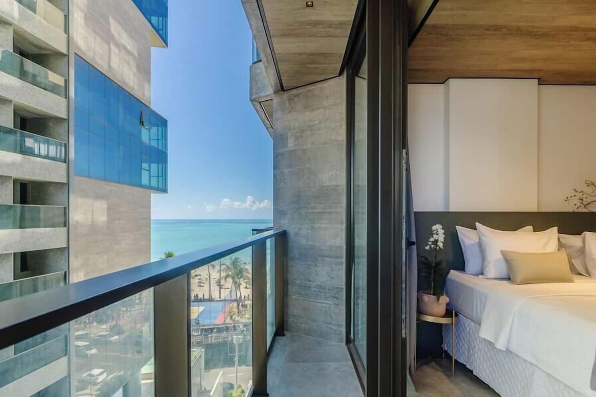 Un dormitorio moderno con una cama grande, vistas al océano y un balcón que da a un paisaje urbano.