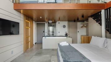 Una habitación de hotel moderna con una cama grande, una kitchenette pequeña, un televisor integrado y un balcón con barandilla de madera.