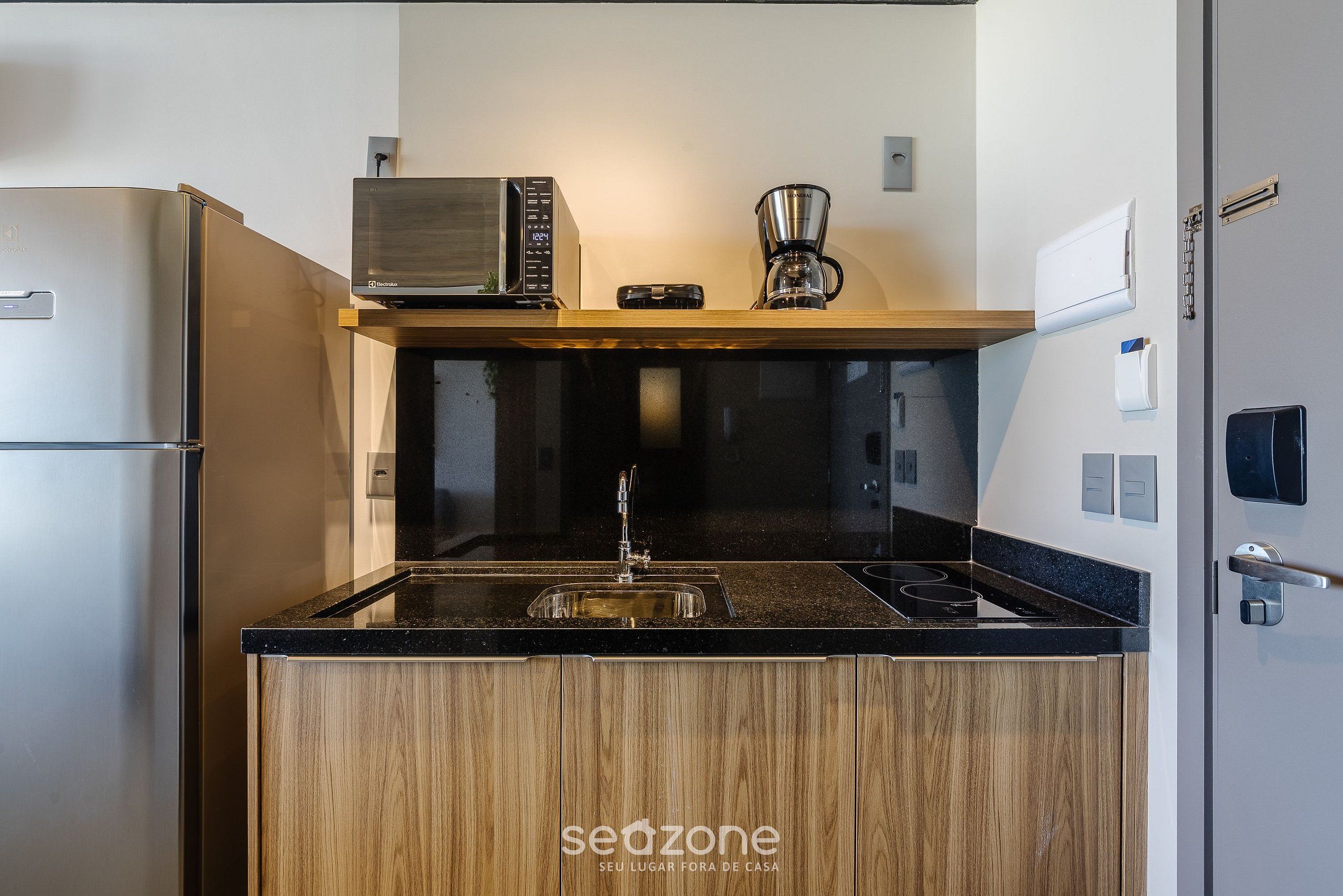Una cucina compatta con frigorifero in acciaio inossidabile, forno a microonde, macchina del caffè e lavello con piano in legno.