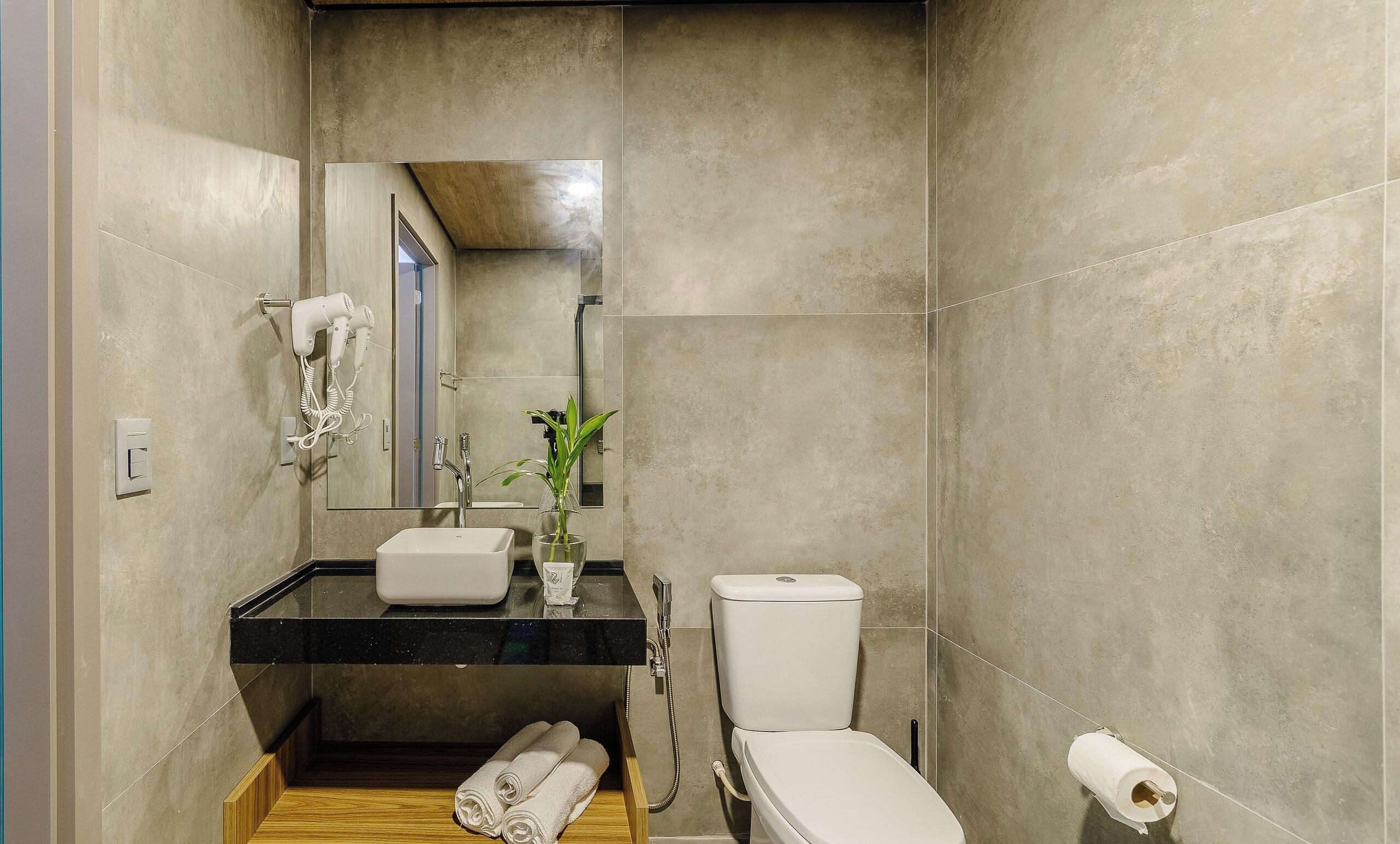 Un baño con inodoro, lavamanos y secador de pelo fijado en la pared.