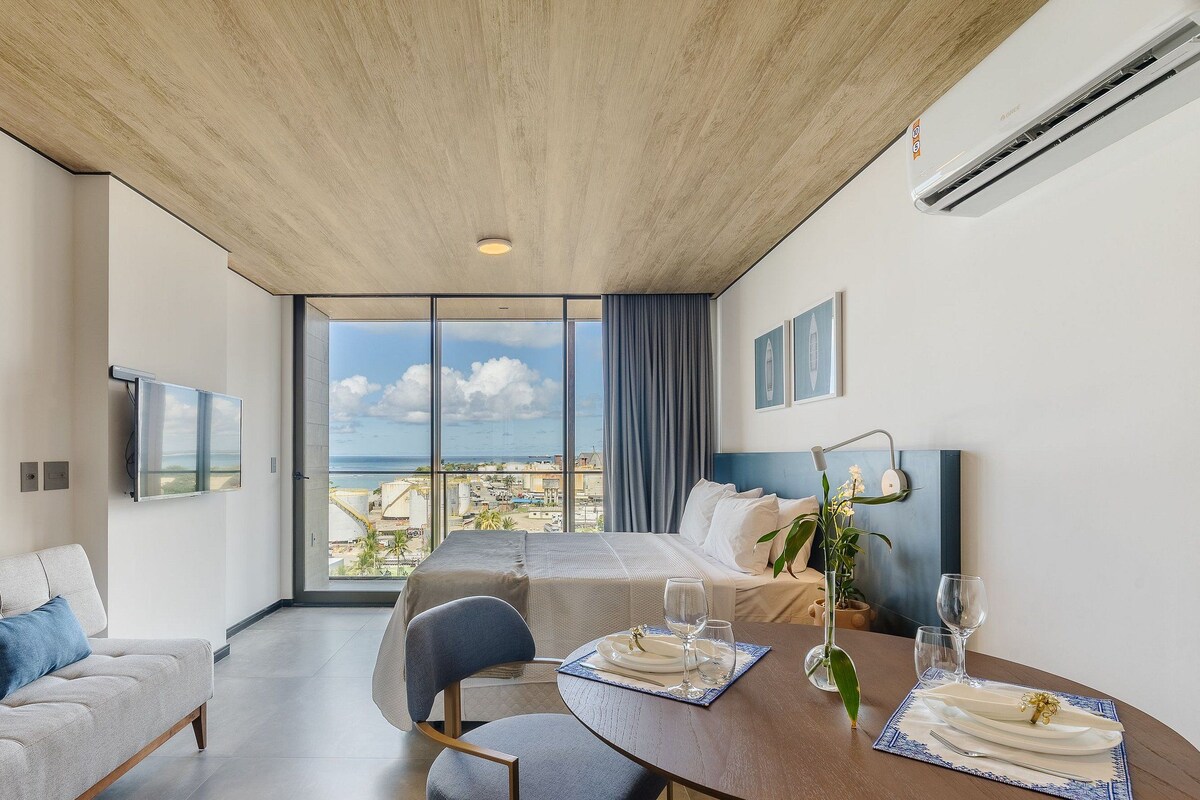 Een moderne hotelkamer met een groot raam, een eettafel voor twee personen, een bank en een bed.