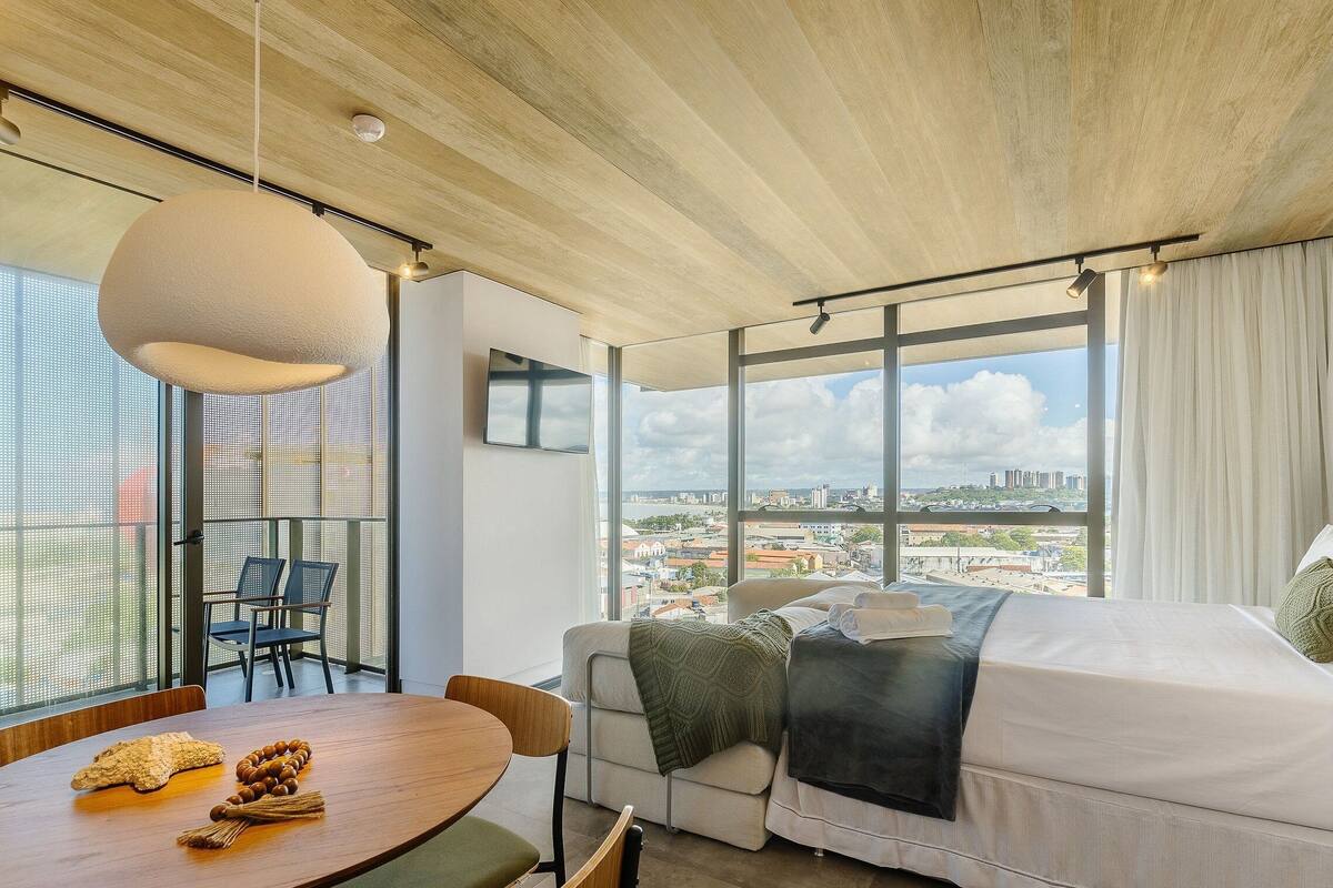 Una habitación moderna con un ventanal grande, un sofá, una mesa de comedor y un techo con vigas a la vista.
