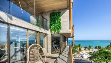 Un edificio moderno con balcón de vidrio con vista a la playa.
