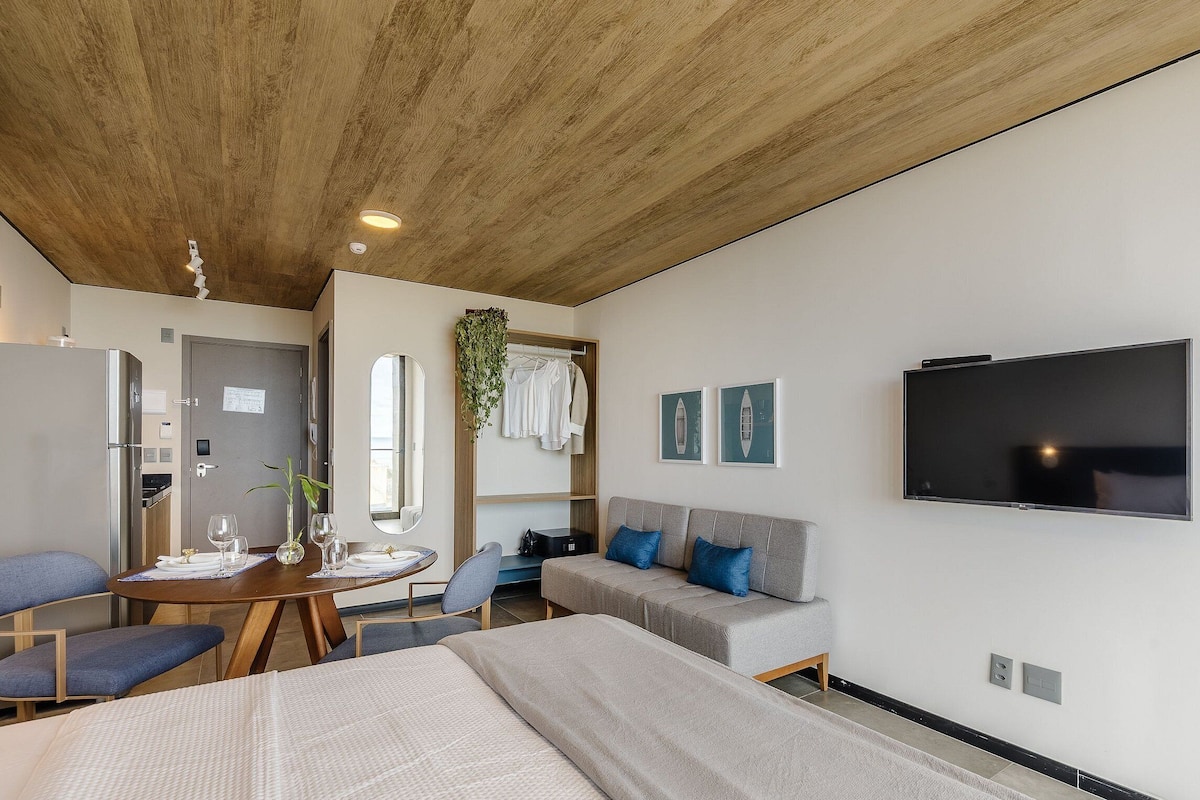 Una habitación de hotel moderna con techo de madera, un televisor de pantalla plana, un sofá, una mesa de comedor con sillas y una cama.