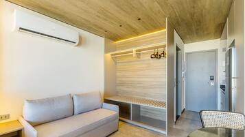A modern hotel room with a wooden ceiling, a sofa, a built-in bench, a coat rack, and a minibar.