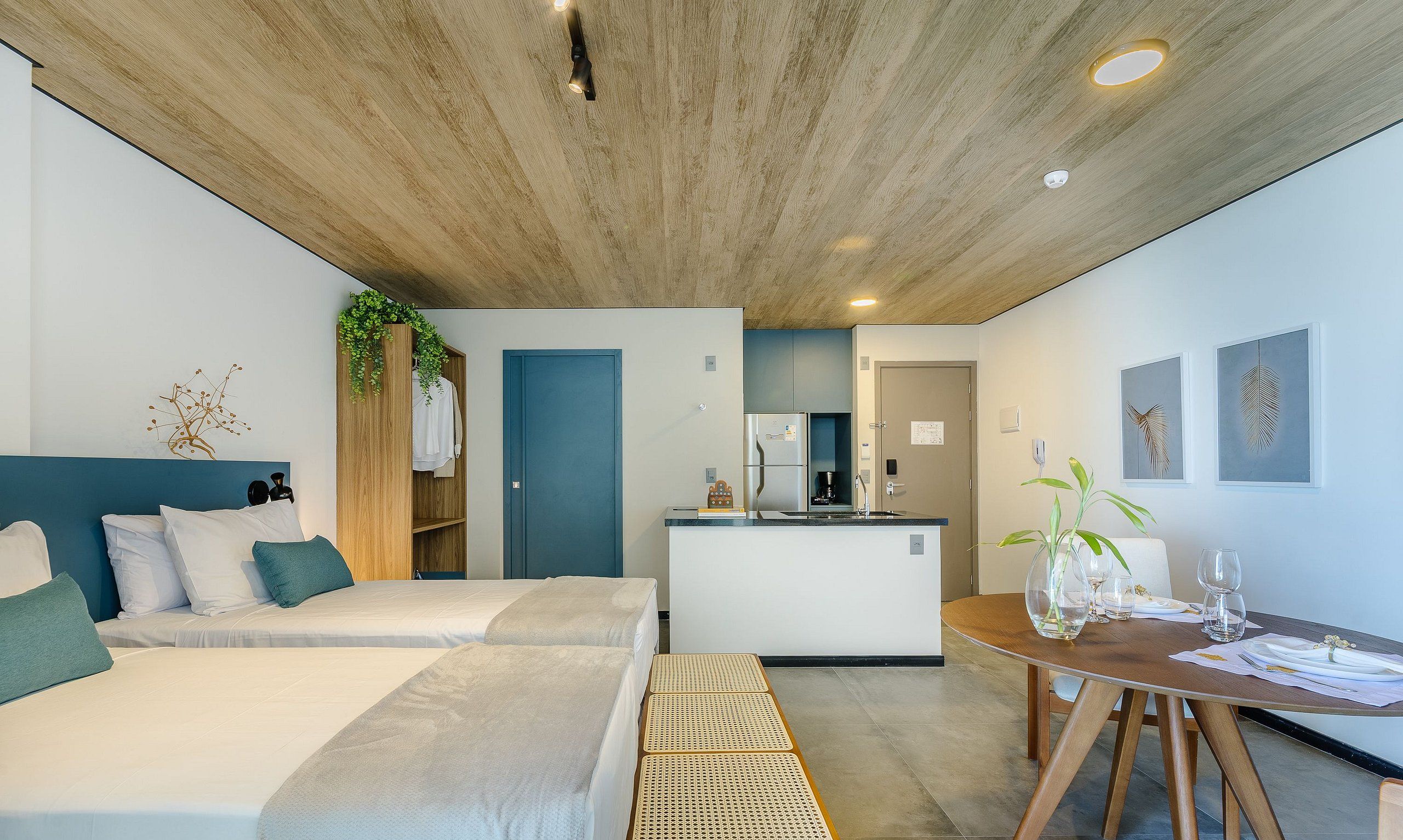 A modern hotel room with a large bed, a small kitchenette, and a dining area.