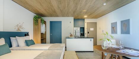 A modern hotel room with a large bed, a small kitchenette, and a dining area.