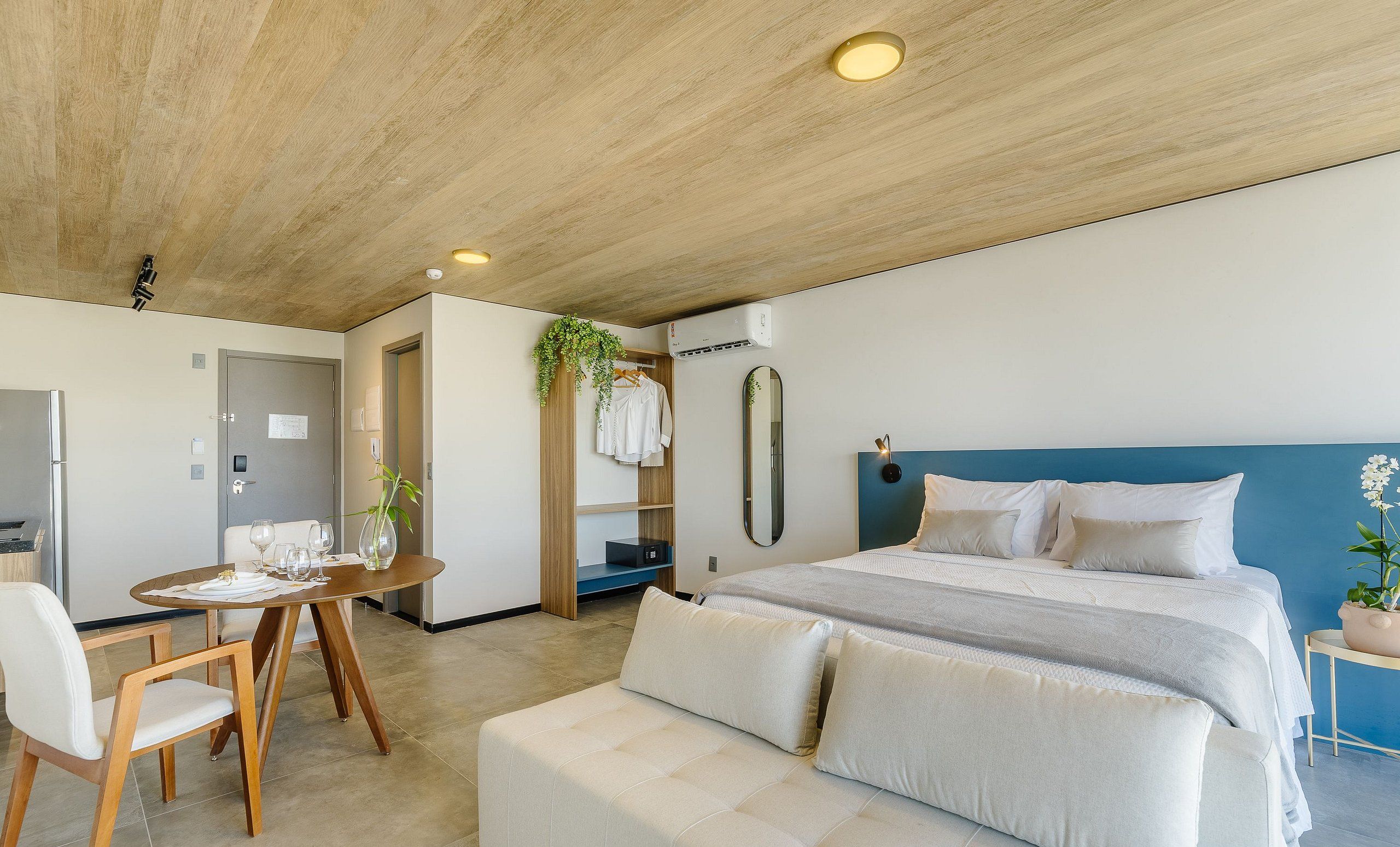 Een moderne hotelkamer met een groot bed, een zithoek met tafel en stoelen, een garderobe en een spiegel.