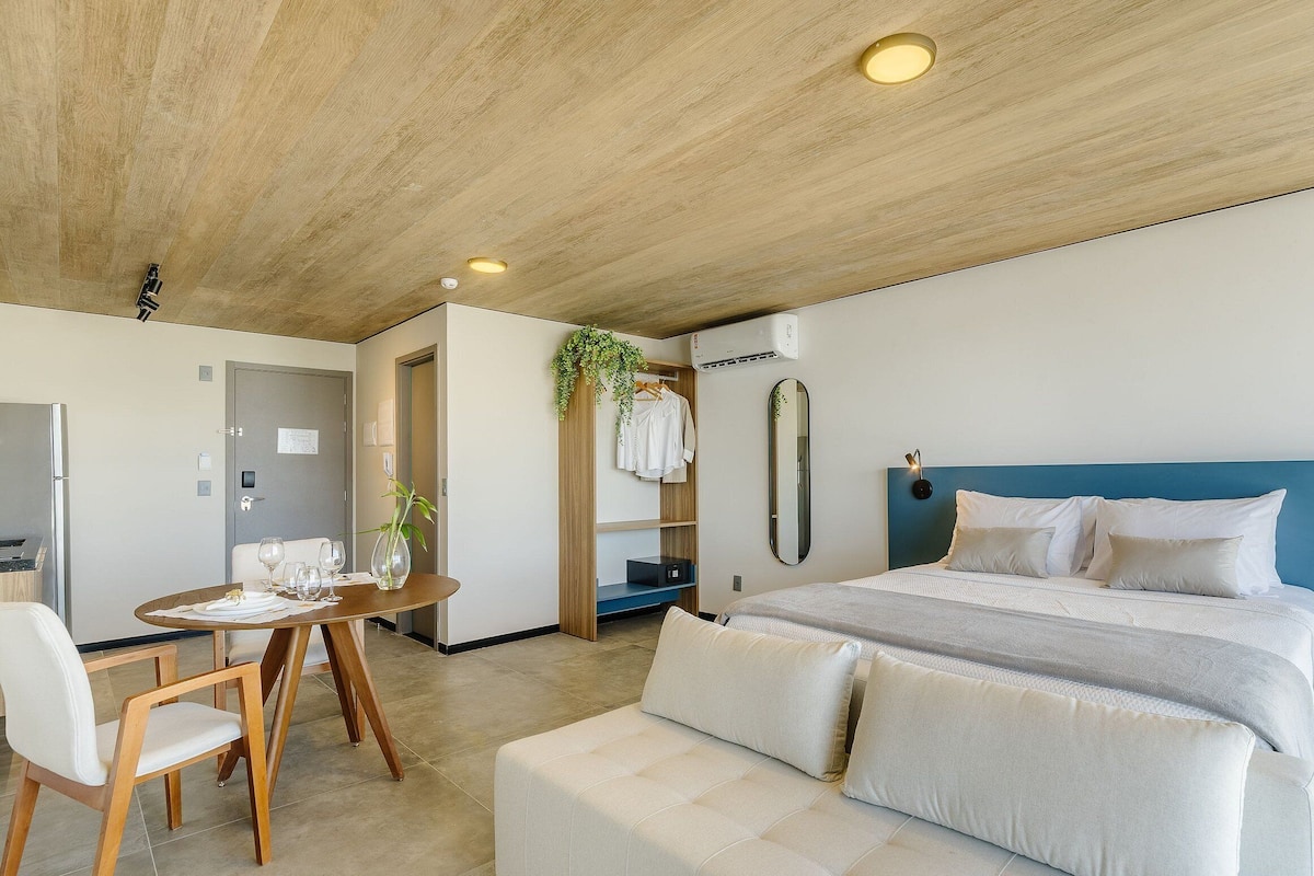 Una habitación de hotel moderna con una cama grande, un área de comedor con mesa y sillas, un armario y un espejo.