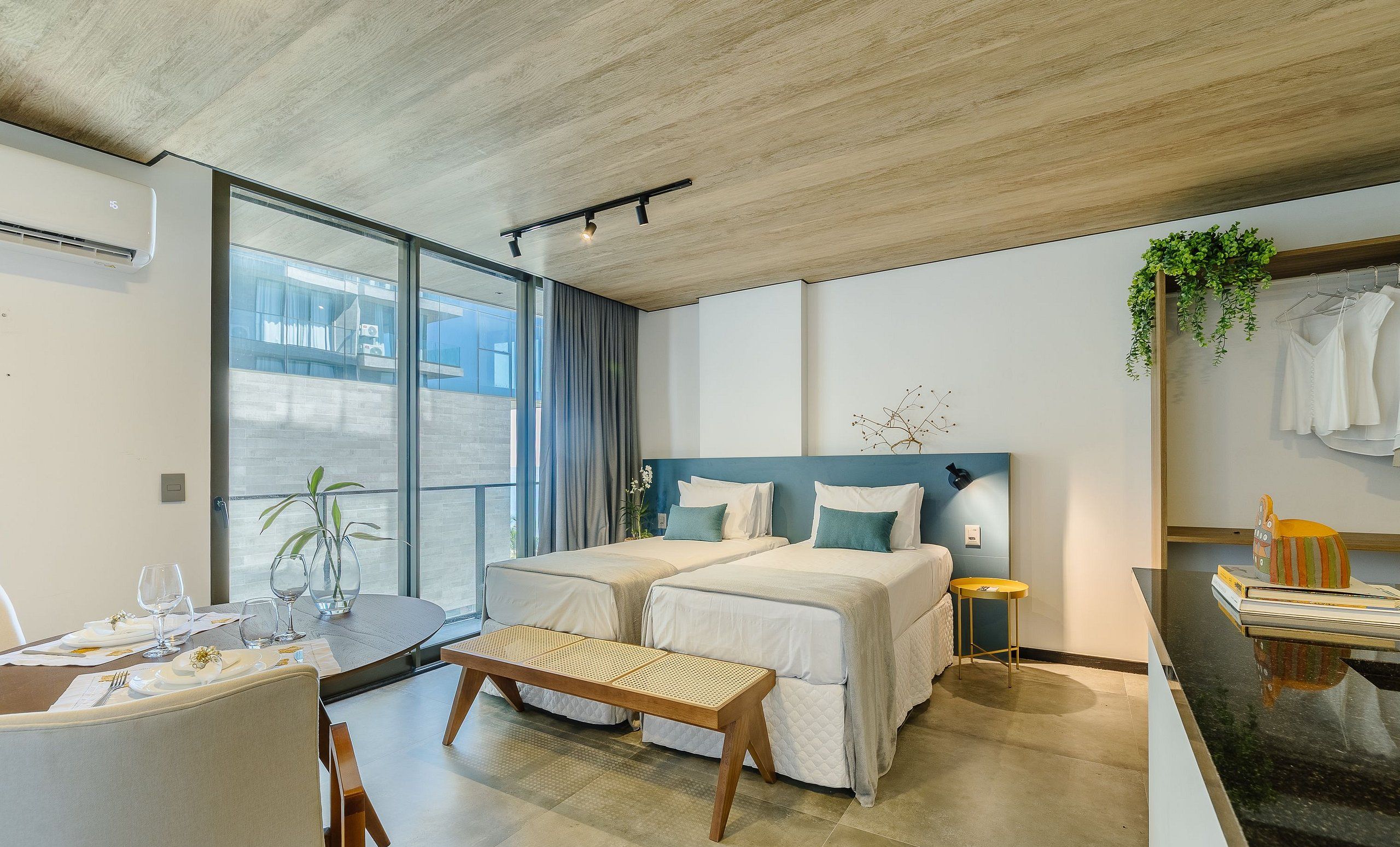 A modern hotel room with a large bed, a small desk, a dining table, and a balcony with a view.